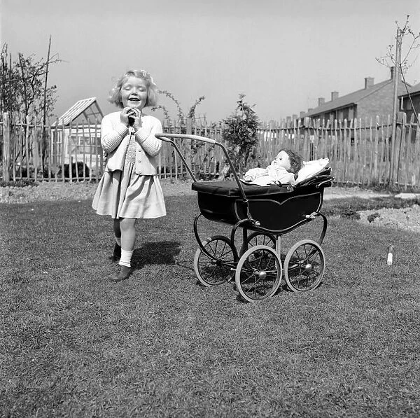 Small girl playing in the garden of her home with a pram and doll. 1954 A228b-002