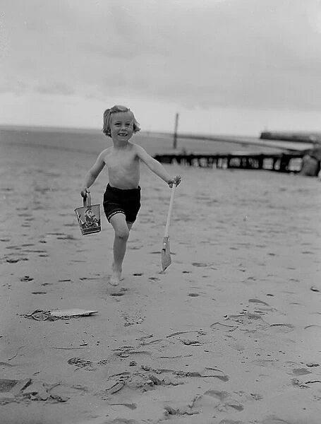 A small girl runs on the beach carrying her bucket and spade enjoying the May Bank