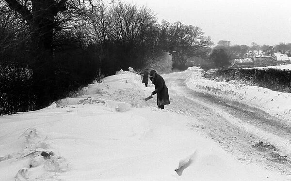 A snowy countryside lane near Coventry. Two men try to clear away the snow