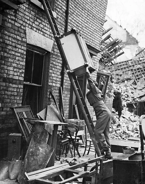 A soldier helping to move luggage from a home that has been hit by the Luftwaffe in The