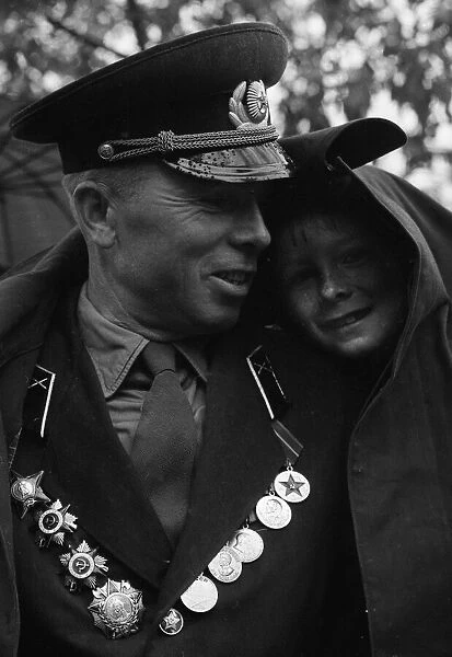 A soldier shelters his son from the rain under his greycoat during the May Day