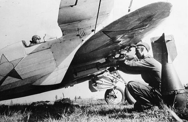 A Soviet pilot sits at his controls while bombs are attached to his aircraft