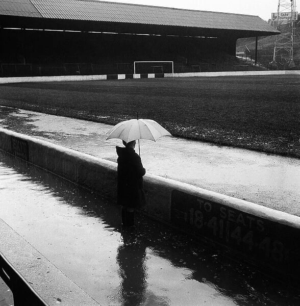 A spectator with an umbrella looks at flooded football ground The Valley