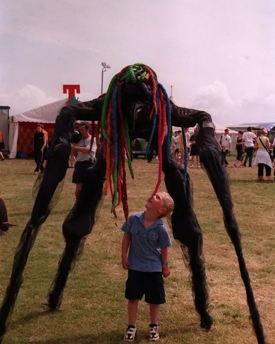 Framed Print : Stilted figure towering over a small boy at T in the Park wearing a bright coloured wig