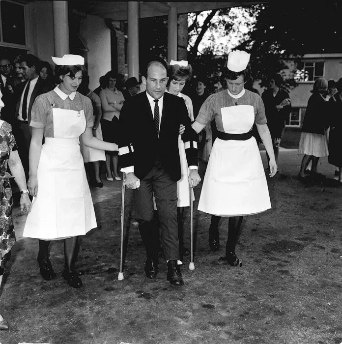 Framed Print : Stirling Moss motor racing driver leaving hospital 1962 on crutches with help of