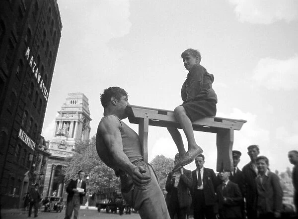 A street entertainer at Tower Hill, London, holding the weight of a boy sitting on a