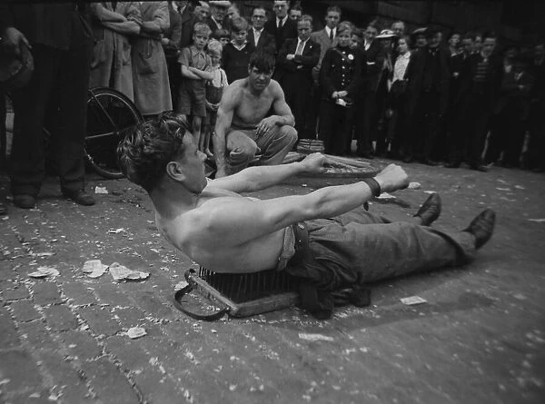 A street entertainer at Tower Hill, London lying on a board of nails watched by a crowd