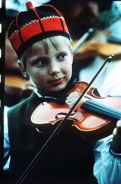 Sweden boy playing violin wearing red and blue traditional hat circa 1990