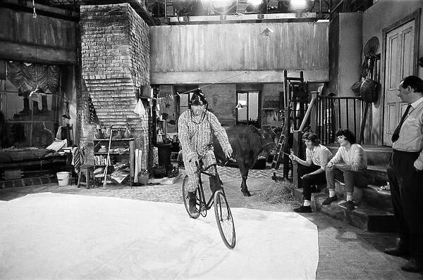 Tony Hancock rides a bike around the set as he films The Rebel at Elstree