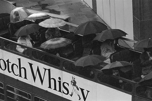 Tourists sit underneath their umbrellas on the top deck of an open top bus during a