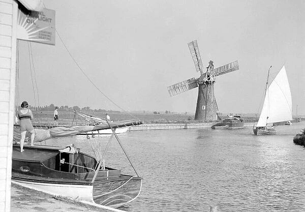 Traditional Norfolk Broad yachts sailing past one of the many windmill water pumps that