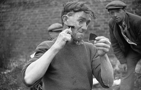 Tramp uses a fragment of a mirror to aid him in his shaving. Circa 1936