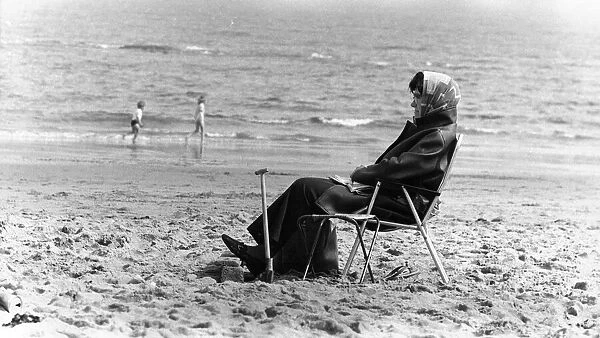 A typical British summer holiday scene, a woman wrapped up in warm clothes including head