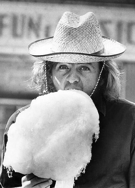 A typical British summer holiday scene, a man wearing a straw hat eating candy floss