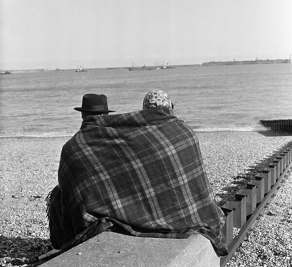 Two visitors to Dover in Kent huddled up on the beach in blankets. 16th April 1954