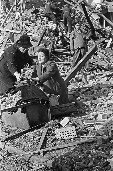 A warden helps a survivor retrieve belongings from the rubble that was her home before it