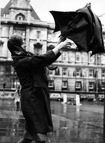 Weather - A young woman struggles with her umbrella during the stormy weather outside