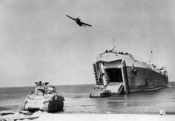 A Wildcat plane passes over a US Navy Landing Ship as it discharges a Sherman tank onto a