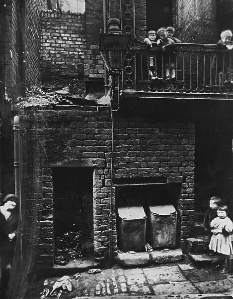 A woman and six children, some on a balcony, in a Liverpool slum scene