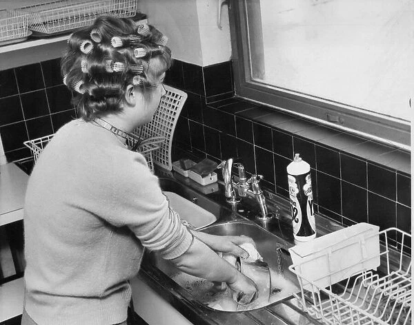 A woman is doing the washing up whislt waiting for her hair to curl before a night