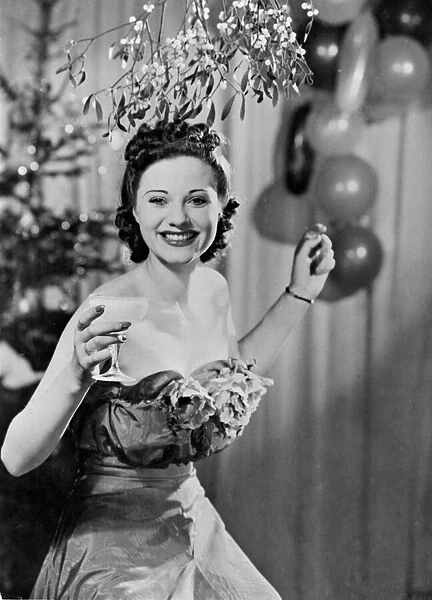 A woman enjoying a drink as she stands under the mistletoe at Christmas time A©