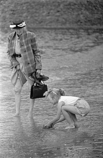 A woman goes for a paddle in the sea as a young gurl picks up a handful of sand
