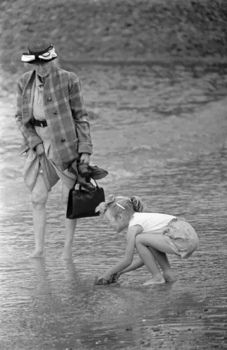 Framed Print : A woman goes for a paddle in the sea as a young gurl picks up a handful of sand