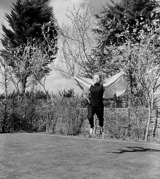 A woman jumping up and down in her back garden on a pleasant Spring day Circa 1954