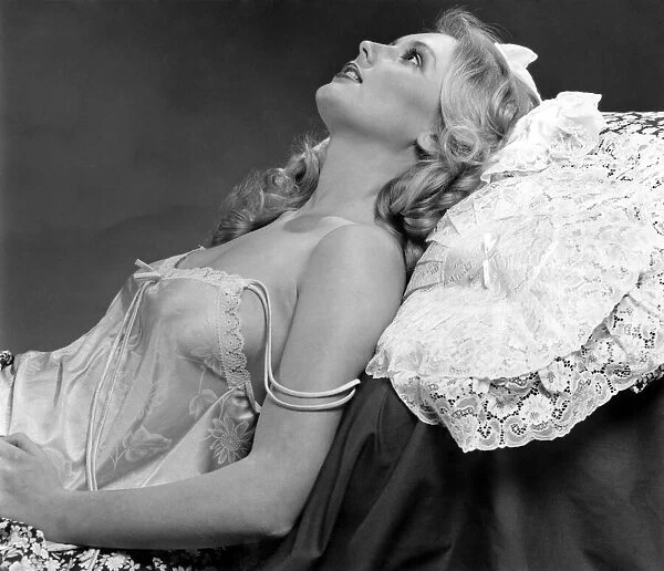 Woman leaning back against a lace pillow wearing a silk nightdress March 1980