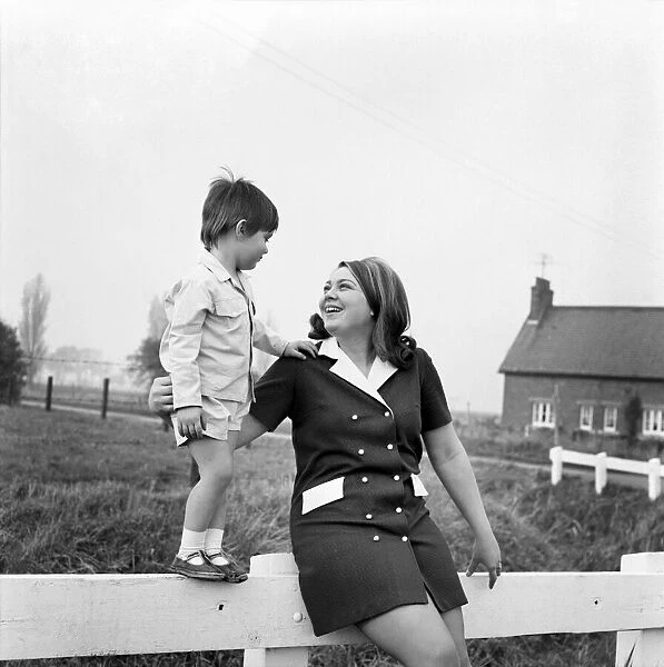A woman outside with her son standing on a gate in a country field November 1969