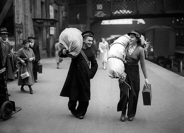 Woman Railway Porter on the station platform carrying luggage for a sailor Circa