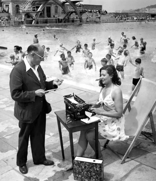 Framed Print : Woman typist working in the sun beside a swimming pool filled with children having fun