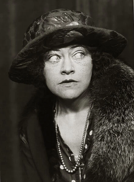 A woman wearing 1920s style clothing including coat, big hat and necklace