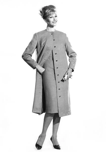 Woman wearing long buttoned coat and dress. Reveille Fashions. Jo Waning