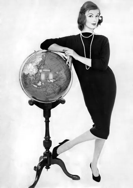 Woman wearing long dress poses leaning against a globe on a stand