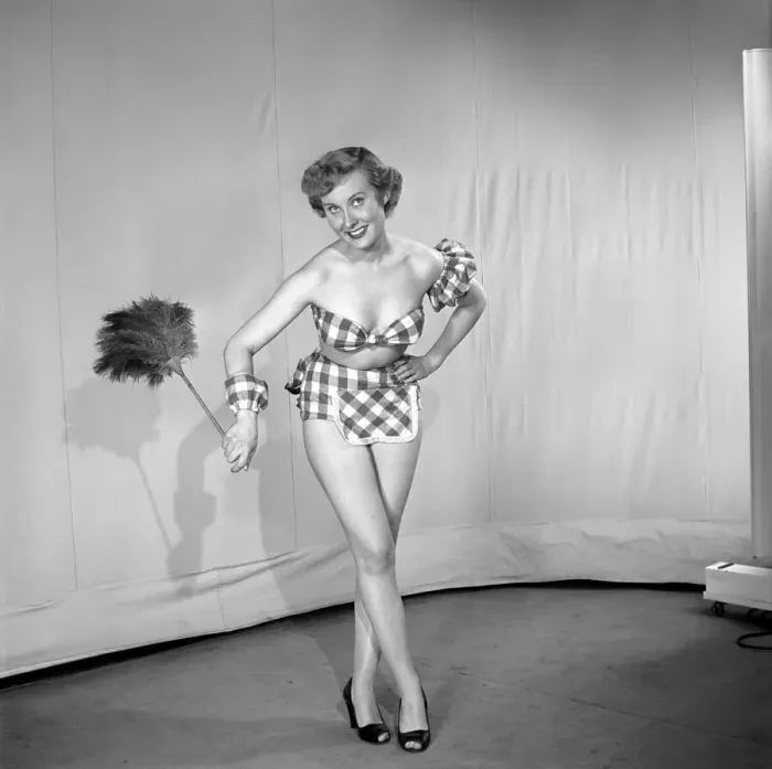 Framed Print : Woman wearing plaid bra and short skirt holding duster. 1959