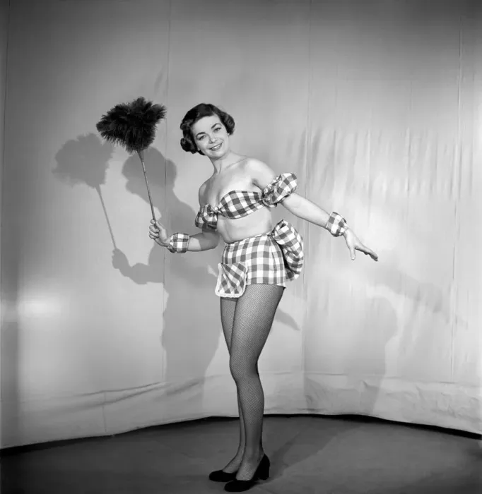Framed Print : Woman wearing plaid bra and short skirt holding duster. 1959