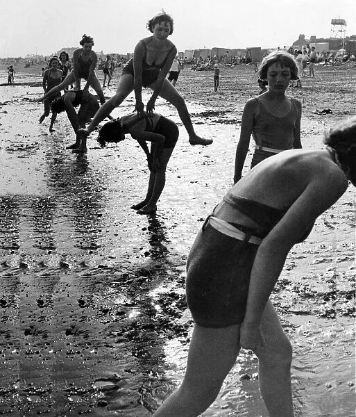 Women and children playing leap frog on the beach. Eastney