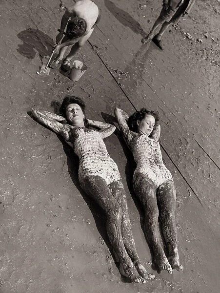 Women Holidaymakers sunbathing on the wet sand wearing swimming costumes bathing suits