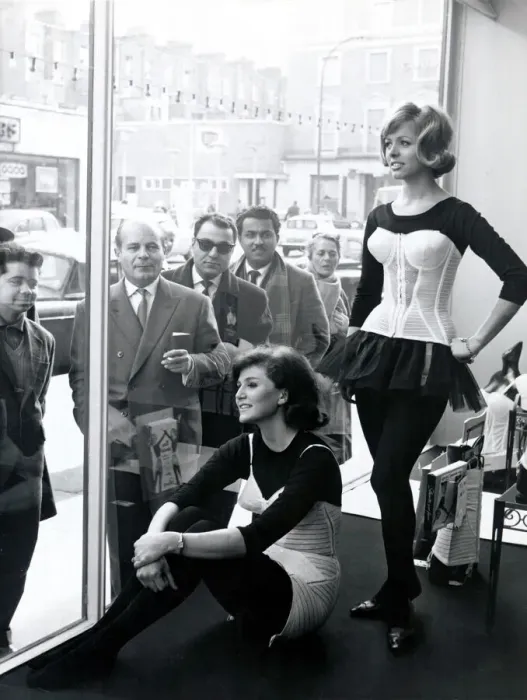 Framed Print : Two women modelling corsets in shop window while people on the street look in - March Framed Print : Two women modelling corsets in shop window while people on the street look in - March