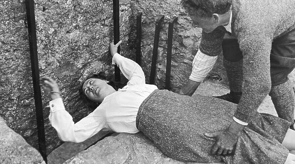 A women seen here with the aid of her gentleman friend kissing the Blarney stone at