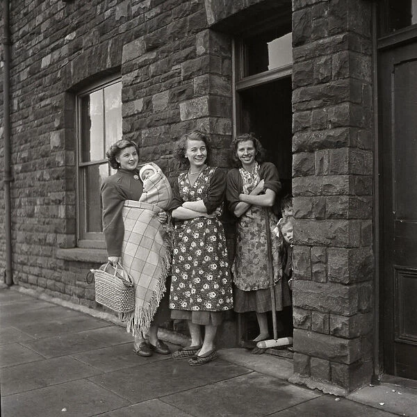Three women standing gossiping on the street outside terraced housing in Cardiff, Wales