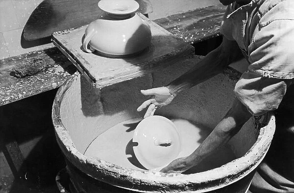 A worker at the Minton China Works in Stoke On Trent, dips a newly created article into a
