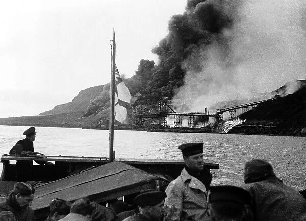 WW2 Allied troops watch from a ship as a German fuel dump of coal & oil burns out of