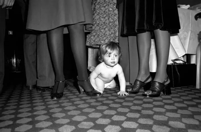 Framed Print : A young baby seen here crawling between the legs of adults at a gathering of them parents