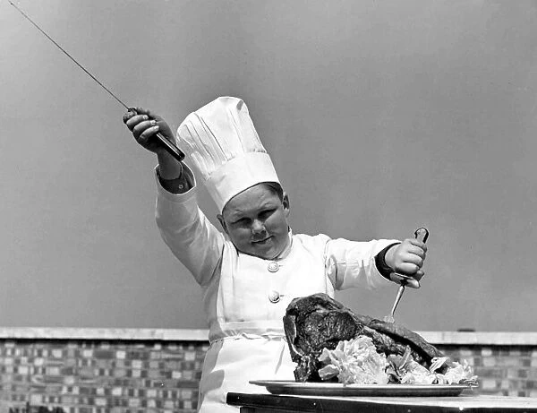 Young boy dressed in a chef uniform including hat, about to carve up a chicken