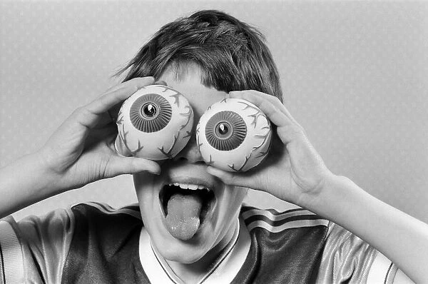 A young boy holding fake eye ball toys up to his eyes. 21st October 1986