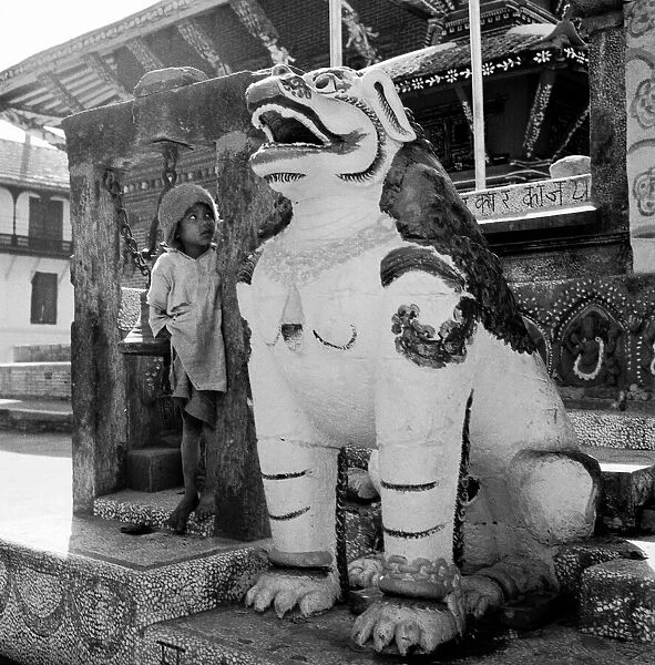 A young boy lookes weary at a statue of a dragon dog guarding one of the buddhist temple