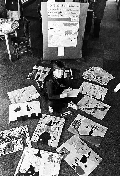 A young boy sitting on the floor among paintings and drawings which have been made by