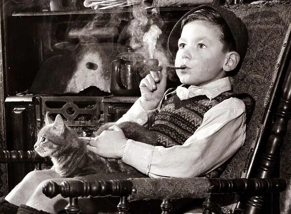 A young boy smoking a pipe and stroking a cat, sitting in a chair looking into